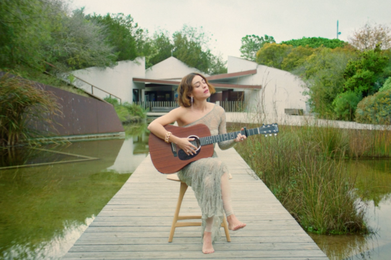 cantante russian red tocando la guitarra en medio de un lago preowned grau